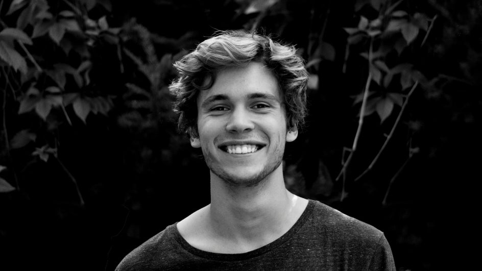 black and white portrait of young man smiling with foliage in background